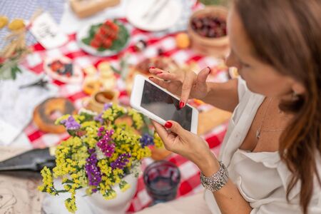 Woman scrolling news on her mobile phone durring outdoor picnic.の写真素材