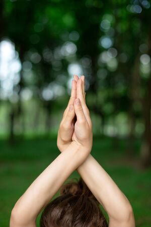 Thin brunette girl plays sports and performs yoga poses in a summer park on a sunset background....
