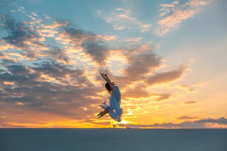 A girl in a fly white dress dances and poses in the sand desert at sunset.の写真素材