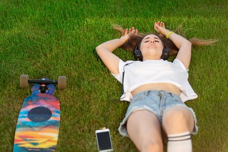 Young girl enjoy lay in green lawn and listening music after riding on her logboard.の写真素材