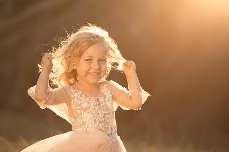 Portrait of a beautiful little princess girl in a pink dress. Posing in a field at sunset.の写真素材