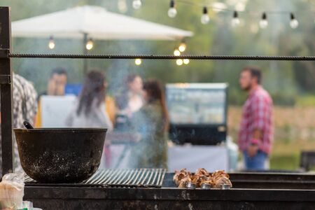 The cook fries juicy steaming meat on a charcoal grill. Food and cooking equipment at a street food festival.の写真素材