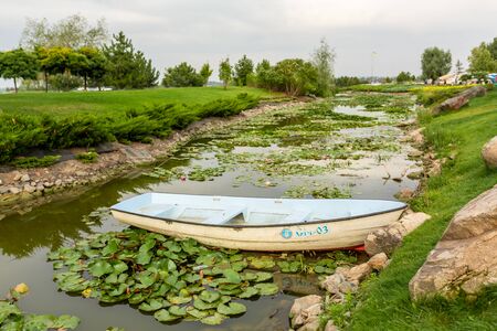 A narrow river channel in which a lotus blooms and a boat stands. Around the green lawns and landscaped area.の写真素材