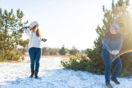 Loving couple play snowballs in winter in the forest. Throw each other snow. Laugh and have a good time.の写真素材