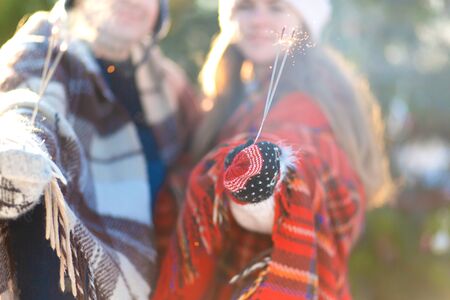 A loving couple in warm plaids kisses holding sparklers in their hands. Meet the winter holidays in...