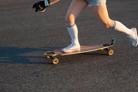 Girl's legs are on the longboard, she rides. Walk on the logboard at the weekend. Girl's feet stand on the board. Background. Copyspace.の写真素材