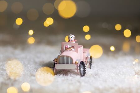 Decorative figurines of a Christmas theme. Santa statuette rides on a toy car with a trailer for gifts. Festive decor, warm bokeh lightsの写真素材