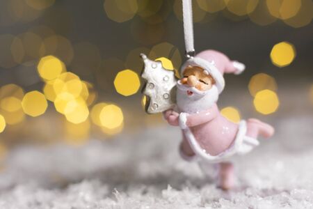 Decorative figurines of a Christmas theme. Santa statuette hugging a small Christmas tree. Christmas tree decoration. Festive decor, warm bokeh lightsの写真素材
