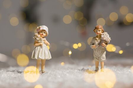 Decorative Christmas-themed figurines. Statuette boy and girl with a bouquet of flowers. Christmas tree decoration. Festive decor, warm bokeh lightsの写真素材