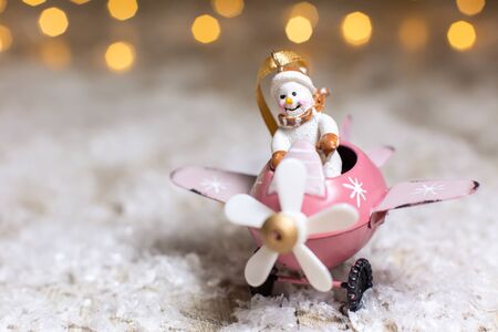 Decorative figurines of a Christmas theme. Snowman in a pink airplane with a propeller. Festive decor, warm bokeh lights.の写真素材