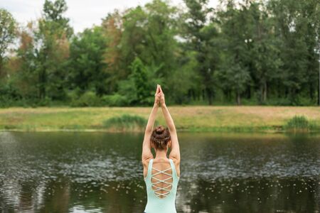 A young sports girl practices yoga on a green lawn by the river, assans posture. Unity with natureの写真素材