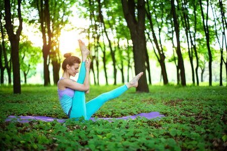 A young sports girl practices yoga in a quit green summer forest, yoga assans posture. Meditation and unity with nature.の写真素材