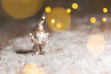 Decorative Christmas-themed figurines. Statuette of a gnome with a white beard and a gift. Christmas tree decoration. Festive decor, warm bokeh lightsの写真素材