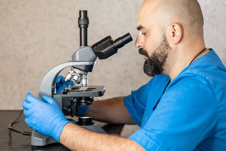Male laboratory assistant examining biomaterial samples in a microscopeの写真素材