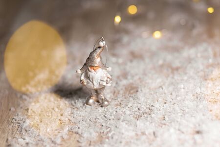 Decorative Christmas-themed figurines. Statuette of a gnome with a white beard and a gift. Christmas tree decoration. Festive decor, warm bokeh lightsの写真素材