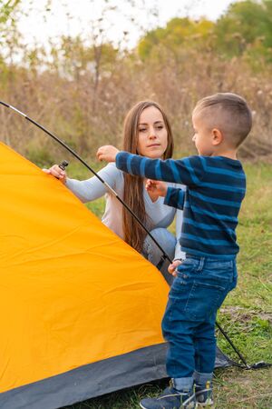 Happy family with little son set up camping tent. Happy childhood, camping trip with parents. A child helps to set up a tent.の写真素材
