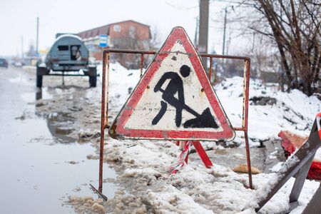 Workers in the municipal utilities repair a broken pipe in the winter. Excavated pit, fenced and with warning signs.の写真素材
