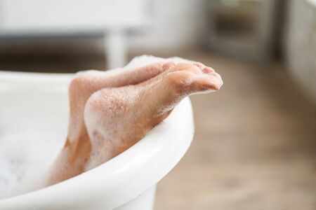 Close-up tender female feet in a white bathtub with soapy foam. Woman enjoying a swim in a bright bathroom.の写真素材