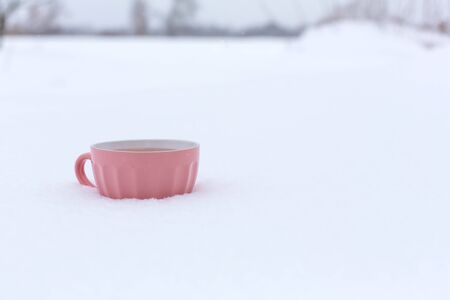 A pink mug with a drink is standing in the snow on a street in winter.の写真素材