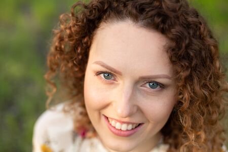 Close up portrait of young smiling attractive woman with curly hair in green flowering spring park. Pure emotionsの写真素材