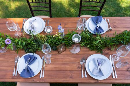 Beautifully decorated wooden table in a summer open-air cafe. Green branch and fresh flowers table decoration.の写真素材