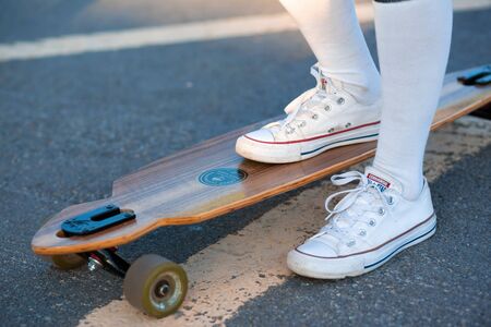 Close up of lady leg in white sneakers resting after extreme funny ride her wooden longboard...
