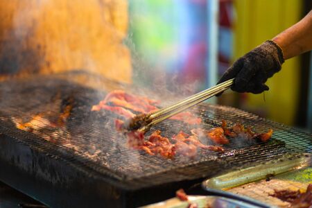 Food seller at night street market in Asia, grilling pieces of meat on the grillの写真素材