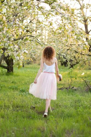 Young attractive woman with curly hair walking in a green flowered garden. Spring romantic mood.の写真素材