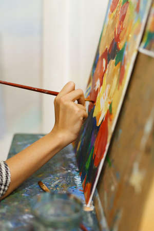 A beautiful blonde girl artist paints a picture on a canvas with oil paints.の写真素材