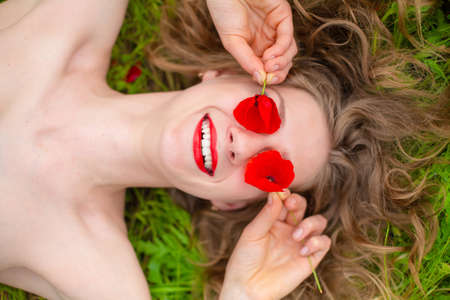A young long-haired girl enjoys the colors of nature on a blooming poppy field on a hot summer day.の写真素材