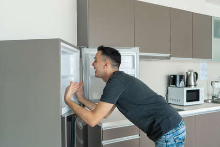 On a hot day, the guy cools with his head in the refrigerator. Broken air conditioner.の写真素材