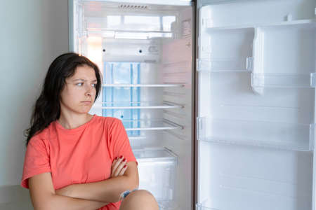 The girl is surprised at the empty refrigerator. Lack of food. Food delivery.の写真素材