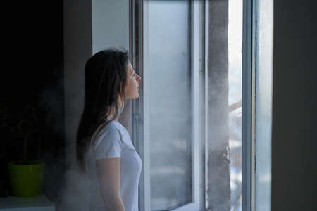 Cold winter weather. Woman step to window, open it and frosty air rushes from outside through open...