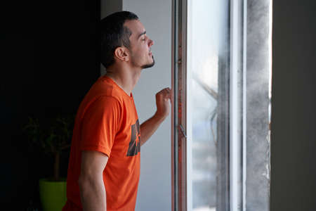 Cold winter weather. man step to window, open it and frosty air rushes from outside through open...