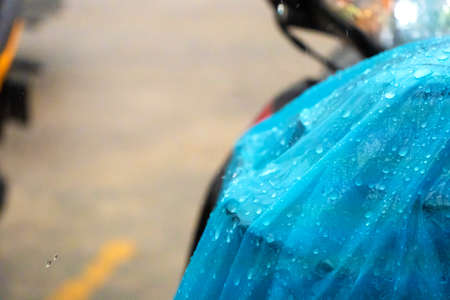A close-up of a raindrop on a blue raincoat thrown onto a scooter during the rain.の写真素材