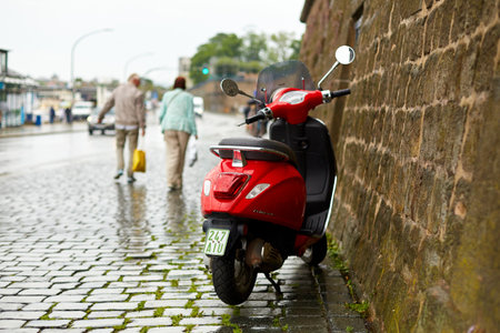 A red scooter is parked against a stone wall, for the duration of the rain. Dresden, Germany - 05.20.2019のeditorial素材