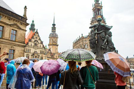 A crowd of tourists with umbrellas in the rain are looking at the monument. A tour in bad weather. Dresden, Germany - 05.20.2019のeditorial素材