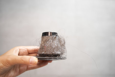 Dirty paper filter of a handheld vacuum cleaner. A man holds a cone filter with dust and hair in a binの写真素材