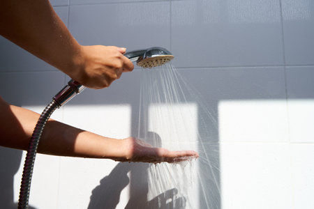 Female hand touching water pouring from a rain shower head, checking water temperature