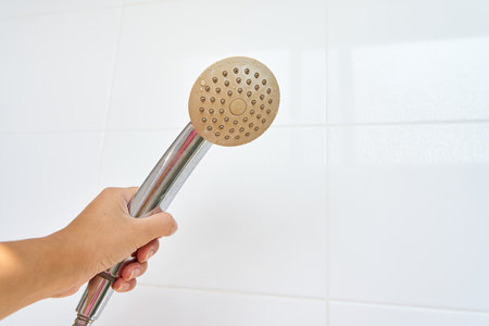 Woman holding in hand corroded limescale calcified old shower head hanging from a stand inside cabin.の写真素材