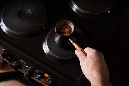 A man preparing black coffee on electric stove. Brew coffee in a Turkish coffee pot.の写真素材