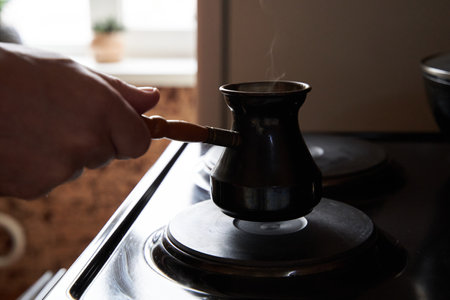 A man preparing black coffee on electric stove. Brew coffee in a Turkish coffee pot.の写真素材