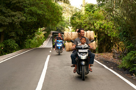 People are riding a heavily loaded motorcycle. Asian people are carrying goods for their small local businesses. Bali, Indonesia - 09/12/2022のeditorial素材