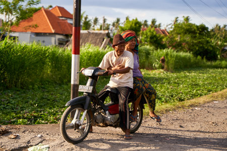 A picturesque local elderly couple riding a motorcycle on a road in a village in Bali. Bali, Indonesia - 10/12/2022のeditorial素材