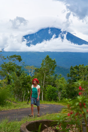 An old Asian woman drives on a road in the mountains with a view of the popular holy volcano Agung, shrouded in clouds on the island of Bali. Bali, Indonesia - 12.24.2022のeditorial素材