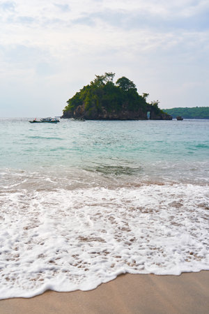A view of the stormy pre-rain ocean washing the sandy beach with waves. A small green island in the seaの写真素材