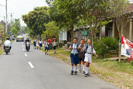 A group of children in uniform walk from school along a road in an Indonesian village in Asia. Bali, Indonesia - 03.22.2018のeditorial素材