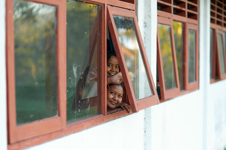 Happy little girls smile and look out of the window of a village school on the popular tourist island of Bali. Bali, Indonesia - 03.10.2018のeditorial素材