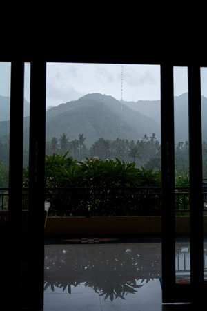 A tropical rainstorm in a rice field with cascading mountains and palm treesの写真素材