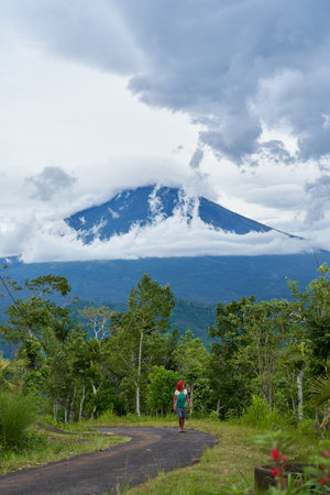An old Asian woman drives on a road in the mountains with a view of the popular holy volcano Agung, shrouded in clouds on the island of Bali. Bali, Indonesia - 12.24.2022のeditorial素材